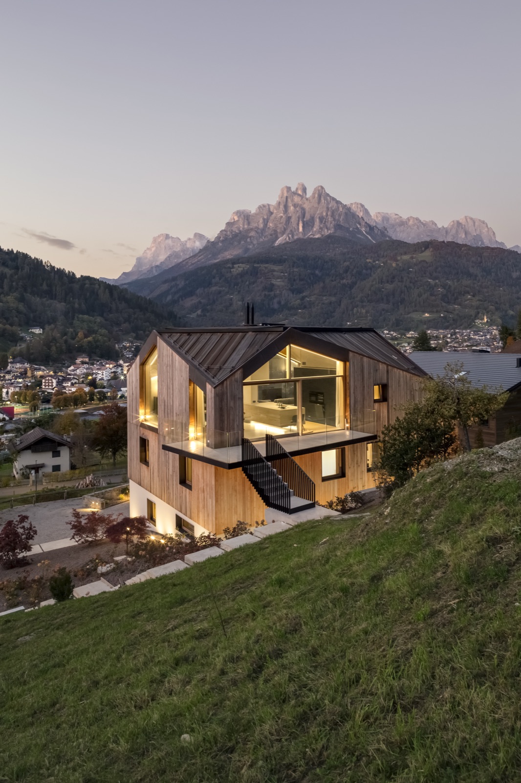 L'architecture en bois de Casa LAGO Dolomiti au crépuscule, ses fenêtres éclairées tournées vers les Pale di San Martino